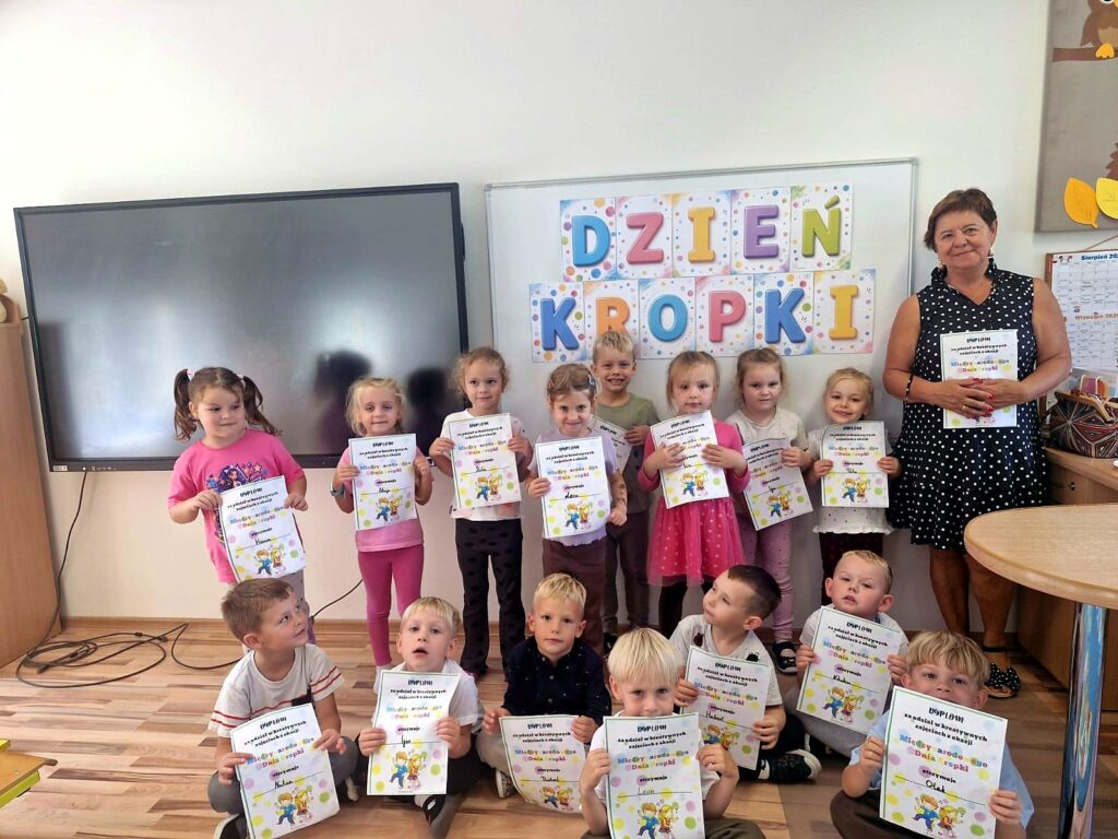 Dzieci z przedszkola z dyplomami przed napisem „Dzień Kropki”