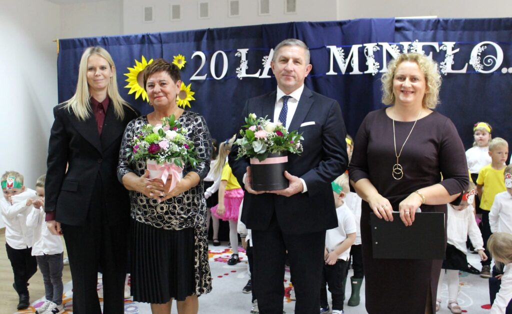 Pamiątkowe zdjęcie uczestników jubileuszu z kwiatami na tle napisu 20 lat minęło.