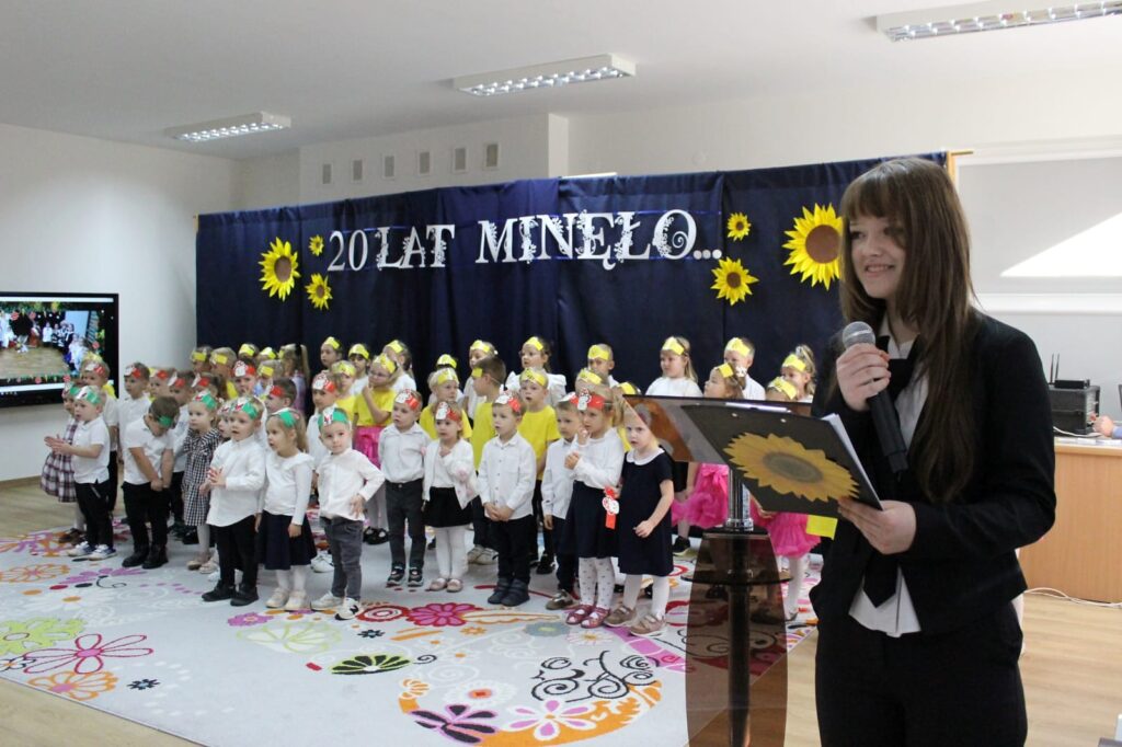 Prowadząca z mikrofonem i przedszkolaki podczas części artystycznej.