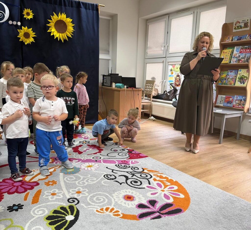 Przemówienie podczas uroczystości w przedszkolu; obok stoją dzieci.