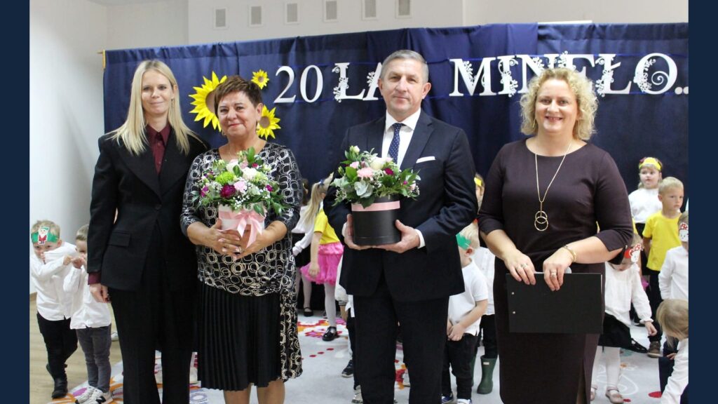 Pamiątkowe zdjęcie uczestników jubileuszu z kwiatami na tle napisu 20 lat minęło.